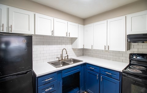 A kitchen with blue cabinets and a black refrigerator.